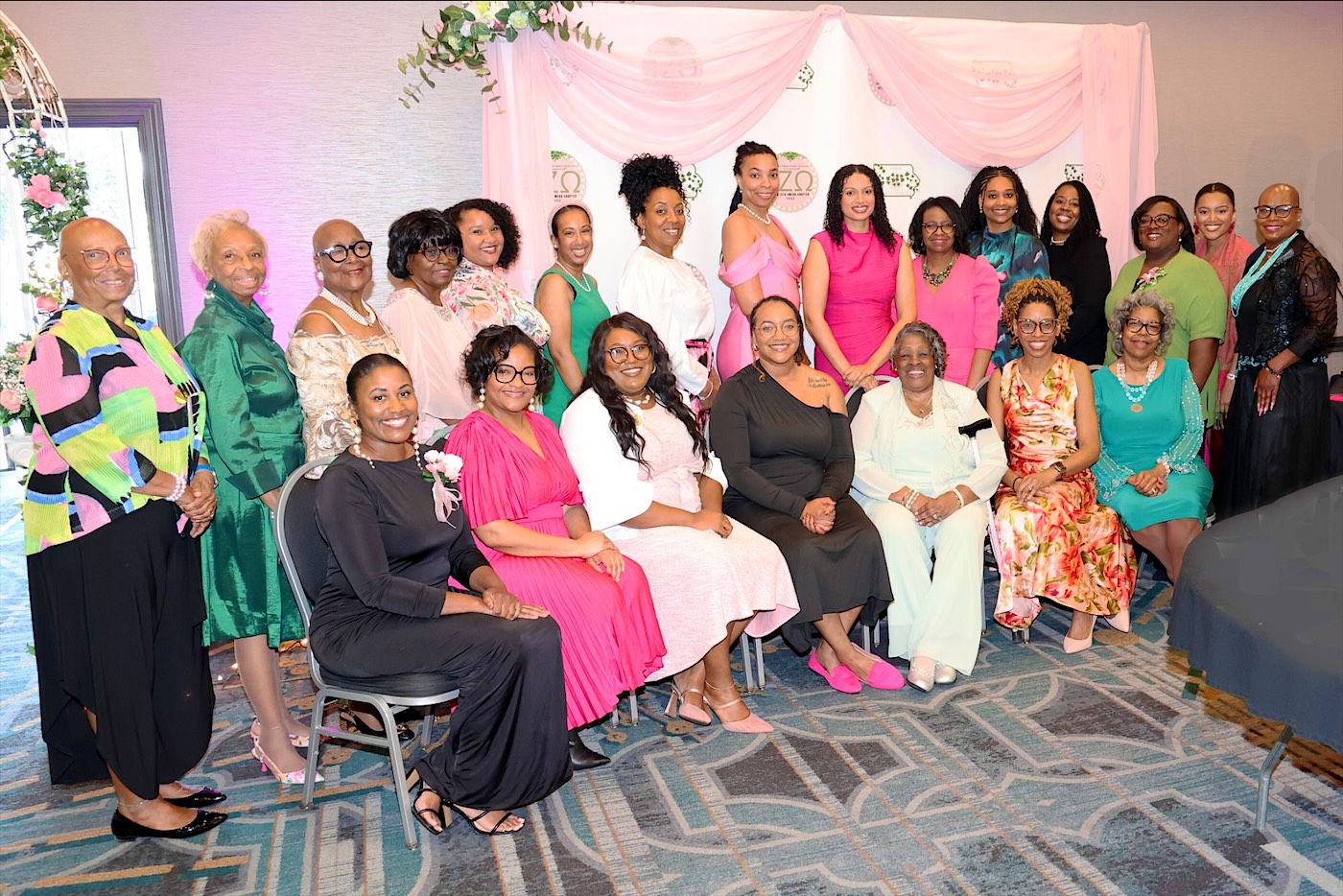 Iota Zeta Omega sorors in pink, green, and white in front of a chapter backdrop